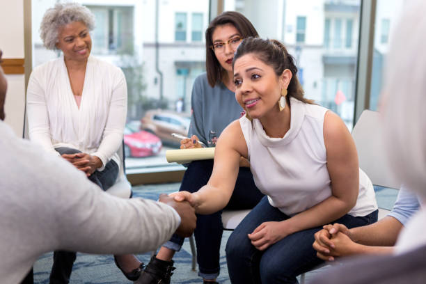 Young businesswoman meets new client A serious young businesswoman sits with colleagues and reaches forward to shake hands with an unseen new client. group therapy stock pictures, royalty-free photos & images