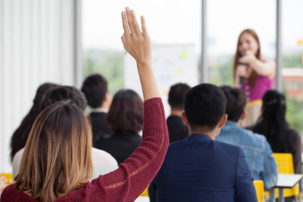 young businesswoman raising hand  to question from Speaker in Seminar. Group Meeting . Conference  Concept . Rear back view stock photo