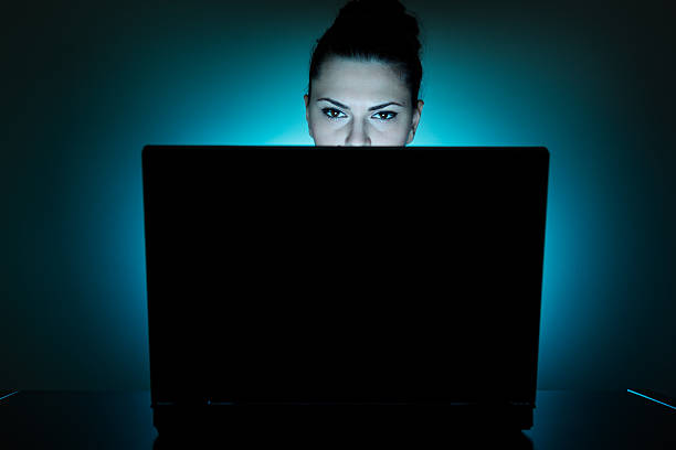 Young businesswoman with laptop at night Beatiful and tired business woman in dark office working on a laptop. Dark circles under eyes visable. staring stock pictures, royalty-free photos & images