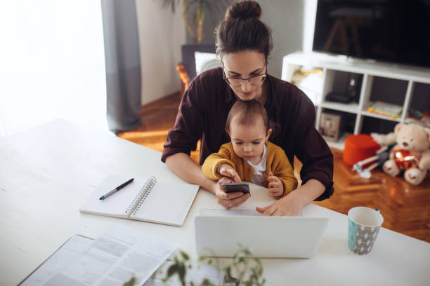 Young businesswoman working from home at her lap top. Young mother drinking coffee at her home office. She working with her child. stock photo