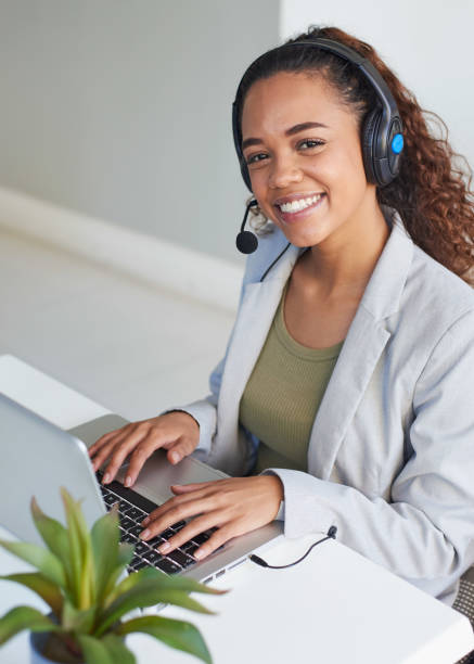 A young call centre agent looks up smiling from her desk while typing stock photo