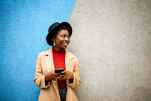 Young casually clothed woman posing in front of coloured wall with smart phone in her hands