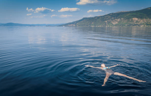 young Caucasian blonde woman swimming in the middle of the lake stock photo