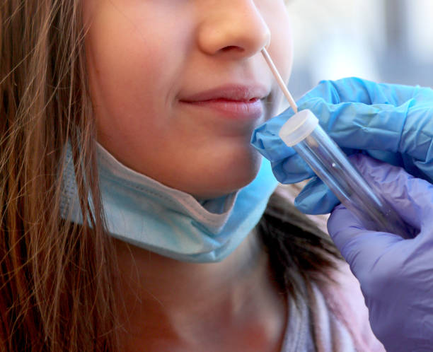 young caucasian girl in the clinic makes a swab in the nose to look for coronavirus and the latex gloves stock photo