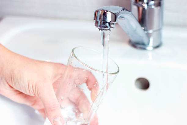 Young caucasian woman hand holding a glass with pure drinking water pouring from home faucet close up stock photo