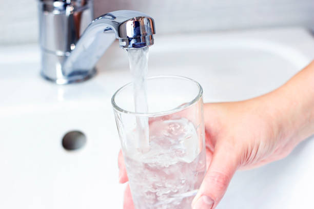 Young caucasian woman hand holding a glass with pure drinking water pouring from home faucet close up stock photo