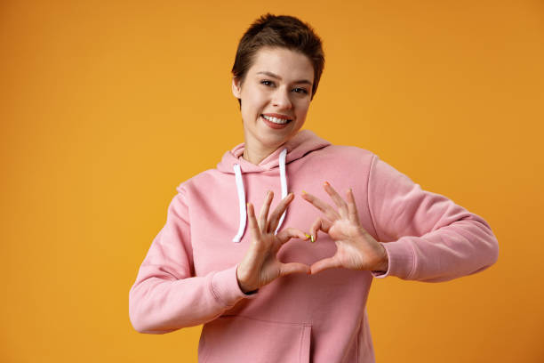 Young cheerful girl showing heart shape sign over yellow background stock photo