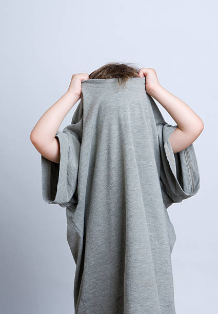 Young child hiding in Daddy's T-shirt A young child hides in Daddy's t-shirt, pulling it up over his head. oversized object stock pictures, royalty-free photos & images