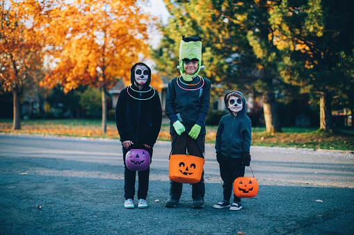 Three young children, two boys and one girl, are dressed as skeletons and Frankenstein for Halloween. They are ready to trick or treat for candy in a local residential neighborhood. Image taken in Utah, USA.