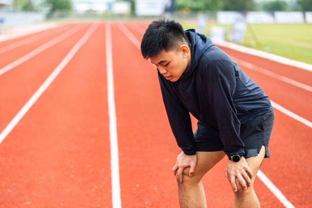 Young chinese man tired during jogging on the track in sport stadium. Young asian male intense training workout challenge breathing exhausted. Healthy and active lifestyle concept. stock photo