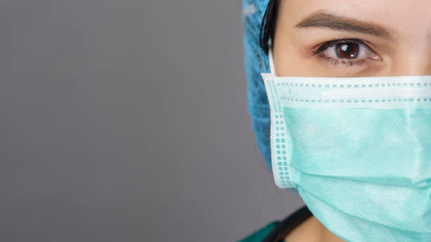joven mujer confiada doctor en exfoliaciones verdes está usando máscara quirúrgica sobre el estudio de fondo gris - nurse face fotografías e imágenes de stock