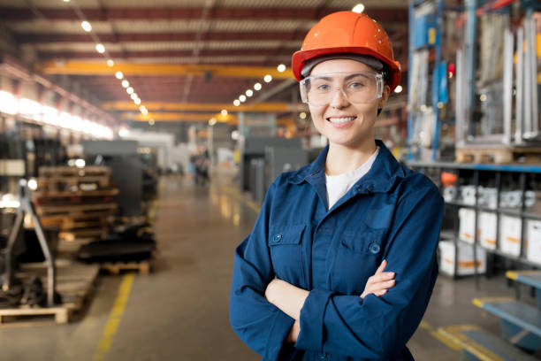 Young controler Young smiling female technician in blue uniform, protective eyeglasses and helmet working in modern factory occupation stock pictures, royalty-free photos & images