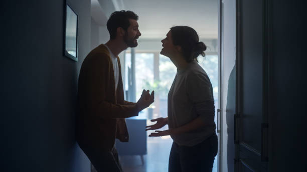 Young Couple Arguing and Fighting. Domestic Violence and Emotional abuse Scene, Stressed Woman and aggressive Man Screaming at Each other in the Dark Hallway of Apartment. Dramatic Scene stock photo