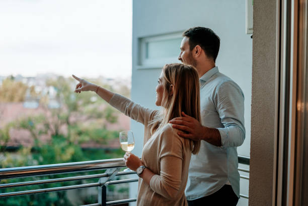 Young couple enjoy drinking wine at balcony. Woman pointing at something. Young couple enjoy drinking wine at balcony. Woman pointing at something. balcony stock pictures, royalty-free photos & images