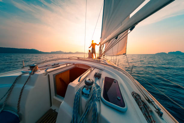 Young couple enjoys sailing in the tropical sea at sunset on their yacht.  yacht stock pictures, royalty-free photos & images