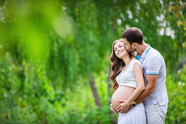 young couple expecting baby outdoors - pregnant couple outside stockfoto's en -beelden