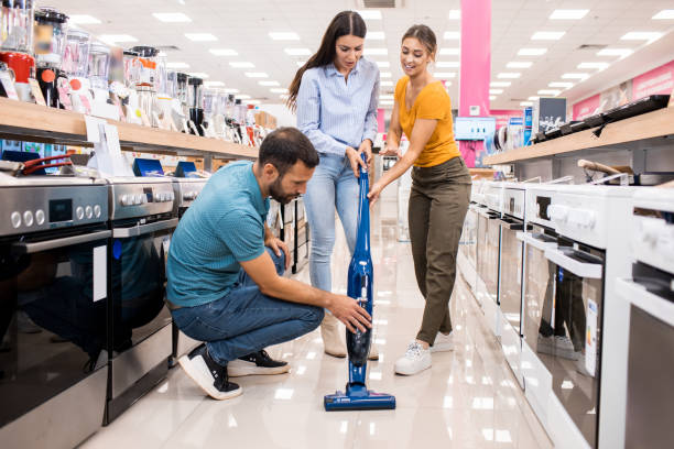 Young couple gets assistance with the vacuum cleaner Saleswoman and a wife are talking while a husband is looking at the vacuum cleaner in a home appliances store. shopping center cleaning stock pictures, royalty-free photos & images