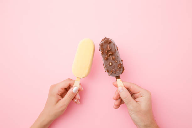 Young couple hands holding together ice creams with dark and white chocolate glaze. Pastel pink color background. Close up. Point of view shot. Top view.  couple eating chocolate stock pictures, royalty-free photos & images