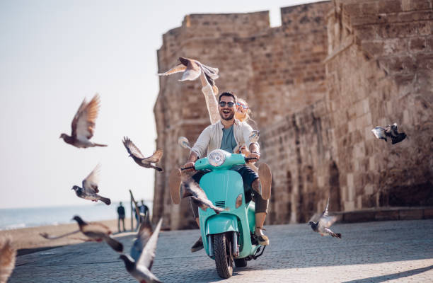 young couple having fun riding scooter in old european town - happy traveling imagens e fotografias de stock