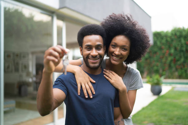 Young couple in front of a house, holding keys of their new home Young couple in front of a house, holding keys of their new home in front of stock pictures, royalty-free photos & images