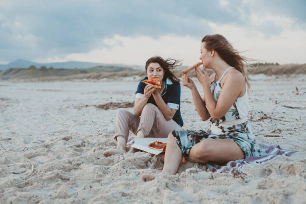 Young couple in love eat pizza on the deserted beach in a summer evening stock photo