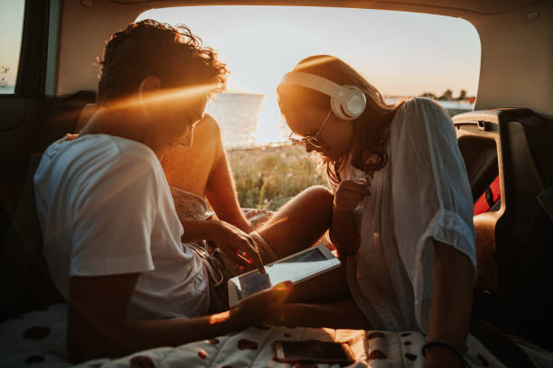 休暇中に車のトランクで若いカップル。背景に海と夕日 - キャンプ　音楽 ストックフォトと画像