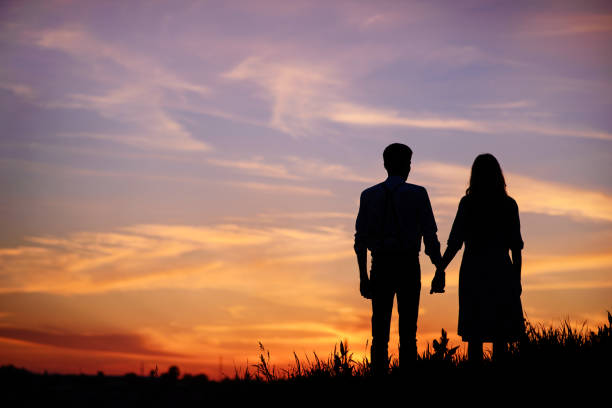young couple is holding hands on a background sunset silhouette stock photo