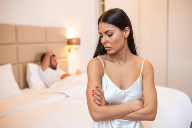 Young couple lying in bed under blanket in bedroom at home, man sleeping, pensive frustrated woman in lingerie thinking about relationships, cheat, treason, family having sexual problems close up stock photo