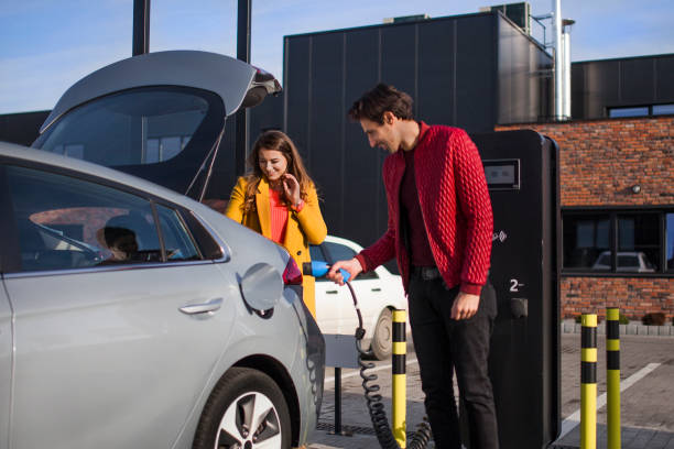 Young couple on a shopping mall parking lot, charging their electric car stock photo