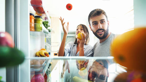 若いカップルは、いくつかの果物や冷蔵庫から野菜を拾います。 - 冷蔵庫　中 ストックフォトと画像