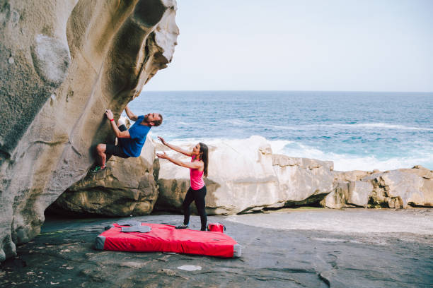 Young couple rock climbing cliffs at the coast helping each other Young couple of climbers assisting eachother to climb the cliff in the coast bouldering stock pictures, royalty-free photos & images