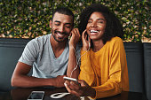 Close-up of a smiling young couple in cafe sharing one earphone and enjoying listening music on mobile phone
