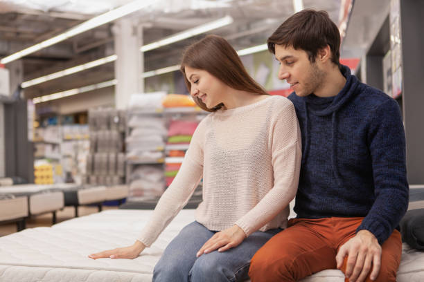 pareja joven comprando en tienda de muebles - tienda de colchones fotografías e imágenes de stock