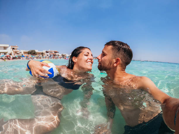 giovane coppia si fa un selfie nella laguna blu del mare - kiss her foto e immagini stock