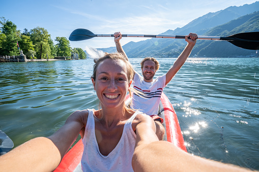 Young couple canoeing take selfie on beautiful mountain lake in Switzerland. 
Inflatable red canoe on water with mountain scenery
People travel outdoor activity concept