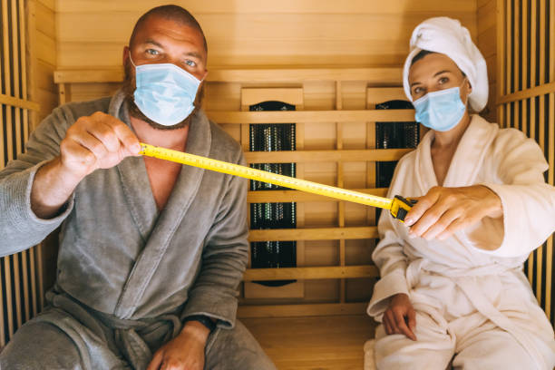 Young couple trying to relax in SPA during corona virus pandemic, using medical face masks and measuring social distance in a small infrared sauna Young couple trying to relax in SPA during corona virus pandemic, using medical face masks and measuring social distance in a small infrared sauna turkish bath photos stock pictures, royalty-free photos & images