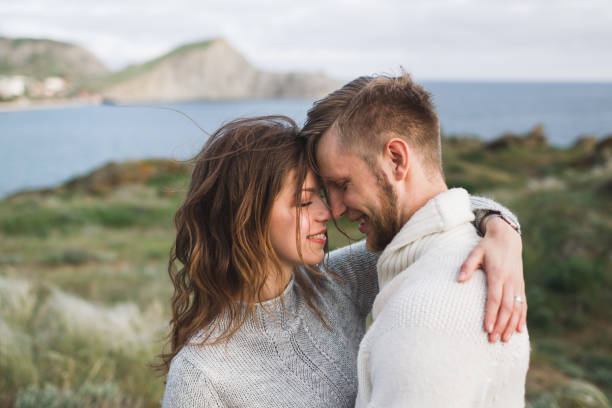 Young couple walking on nordic sea coast with mountain view in spring, casual style clothing sweaters and jeans Young couple walking on nordic sea coast with mountain view in spring, casual style clothing sweaters and jeans sweater photos stock pictures, royalty-free photos & images