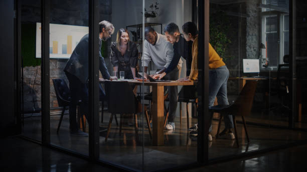 Young Creative Team Meeting with Business Partners in Conference Room Behind Glass Walls in Agency. Colleagues Sit Behind Conference Table and Discuss Business Opportunities, Growth and Development. stock photo