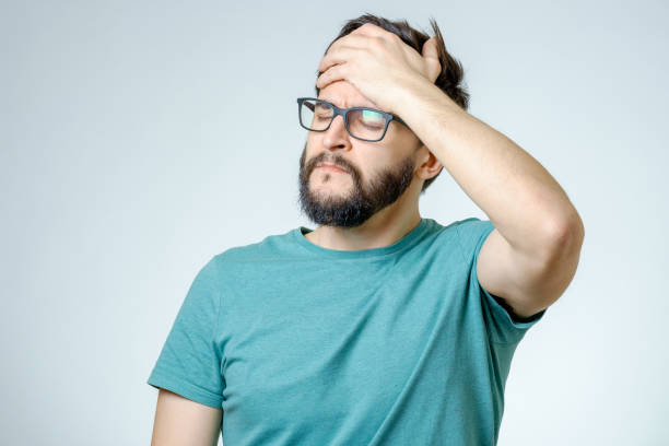 Young depressed handsome bearded man touching his head and having a headache over gray background stock photo