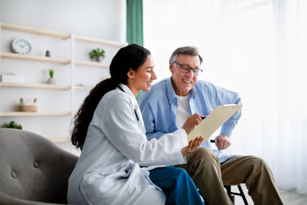 Young doctor asking senior impaired male patient in wheelchair to sign insurance policy at home stock photo