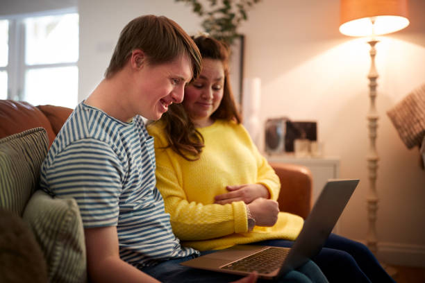 Young Downs Syndrome Couple Sitting On Sofa Using Laptop At Home Young Downs Syndrome Couple Sitting On Sofa Using Laptop At Home adult stock pictures, royalty-free photos & images