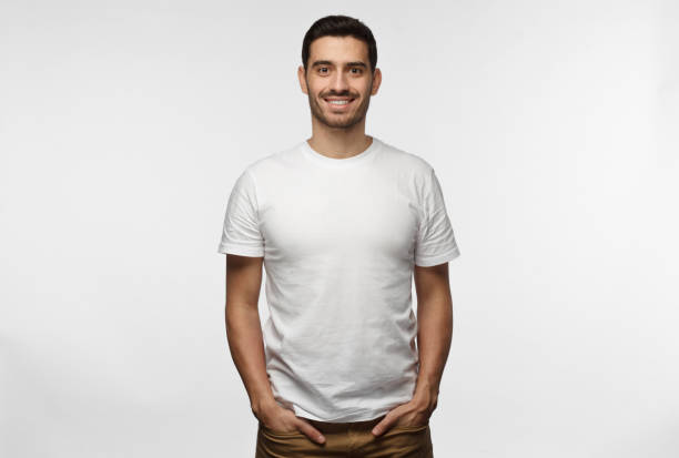 Young european man standing with hands in pockets, wearing blank white tshirt with copy space for your logo or text, isolated on grey background Young european man standing with hands in pockets, wearing blank white tshirt with copy space for your logo or text, isolated on grey background white t shirt stock pictures, royalty-free photos & images