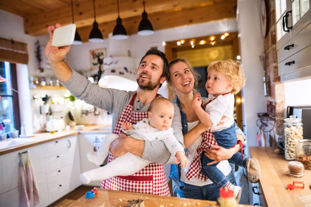 Young family making cookies at home. Beautiful young family making cookies at home. Father, mother. toddler boy and baby taking selfie with a smartphone. tradition photos stock pictures, royalty-free photos & images