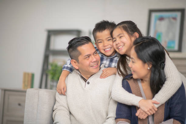 Young Family A family of four are embracing in their living room one afternoon. Everyone is smiling happily. filipino ethnicity stock pictures, royalty-free photos & images