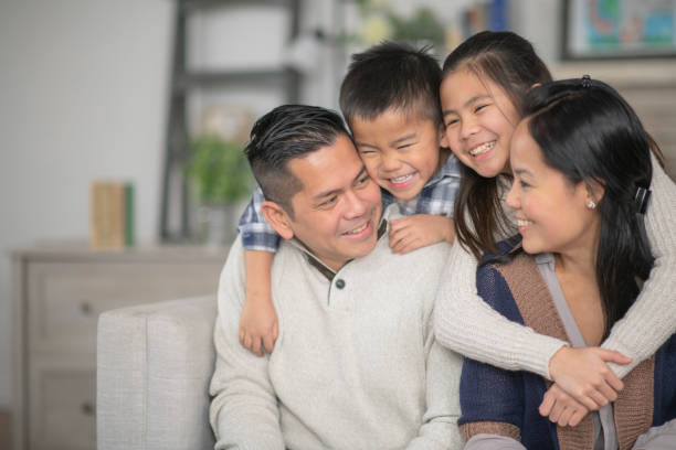 Young Family A family of four are embracing in their living room one afternoon. Everyone is smiling happily. filipino family stock pictures, royalty-free photos & images