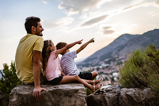Single father and his children relaxing in mountains at sunset.