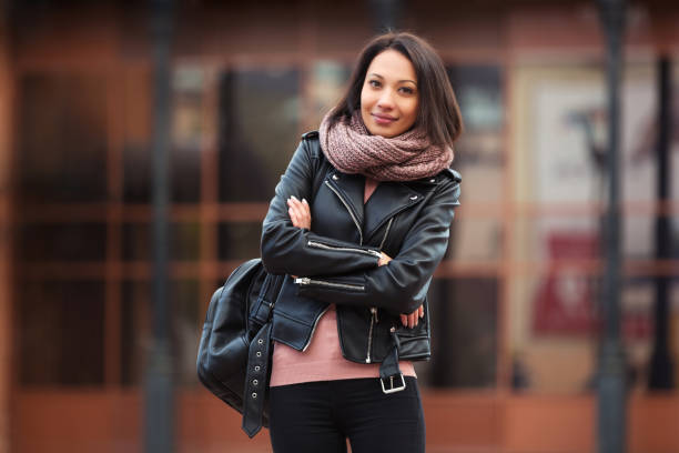 Young fashion woman in black leather jacket walking in city street stock photo