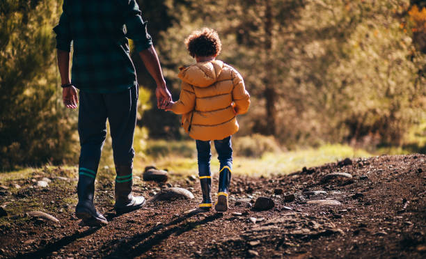 Young father and son with rain boots walking in nature stock photo