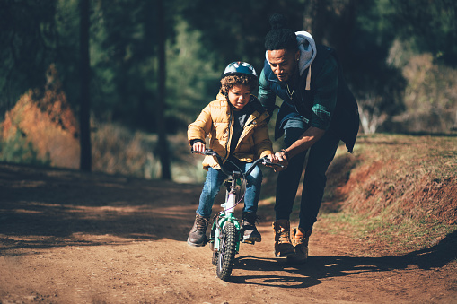 Boy learning how to ride the bike with the help of dad in the countryside