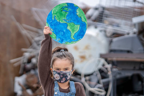 Young female activist Young girl holding a protest sign while standing in front of a large pile of waste. climate change stock pictures, royalty-free photos & images